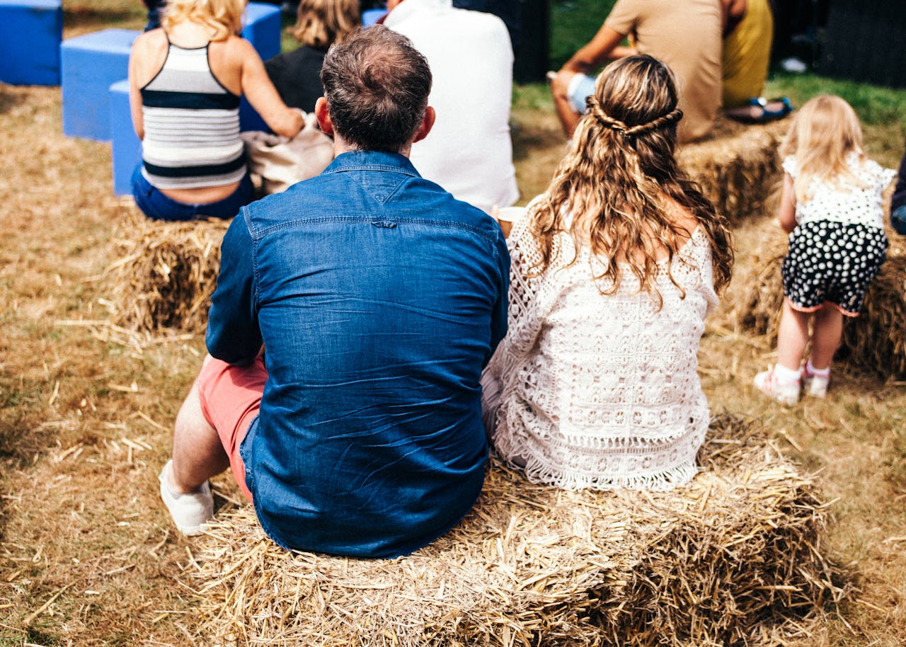 People enjoying an outdoor summer festival sitting on hay bales, Hertfordshire, UK.